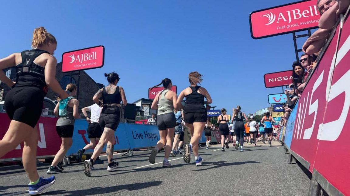 People running down the road while spectators watch from behind the partition