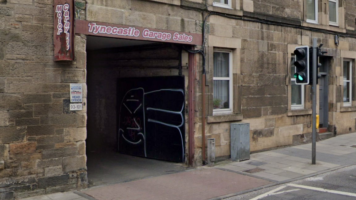 A garage entrance in a sandstone tenement block bears a small sign marking the offices of Capital Cars. 