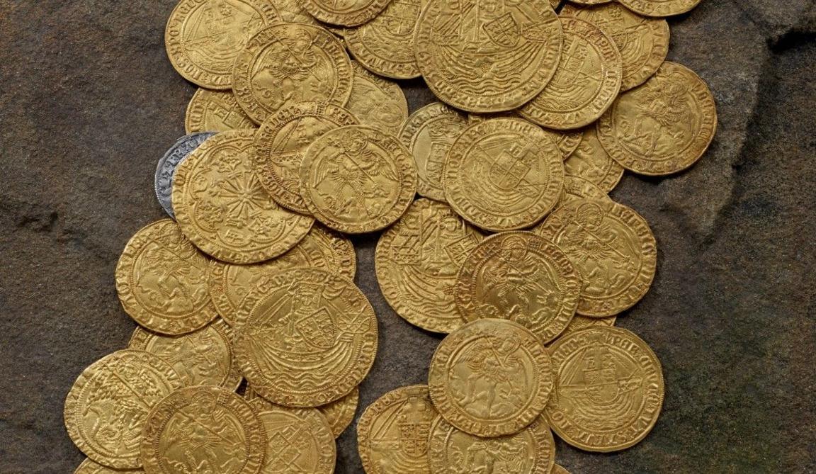 Pile of scattered gold coins and one silver coin seen on the edge of the picture in the top left.
