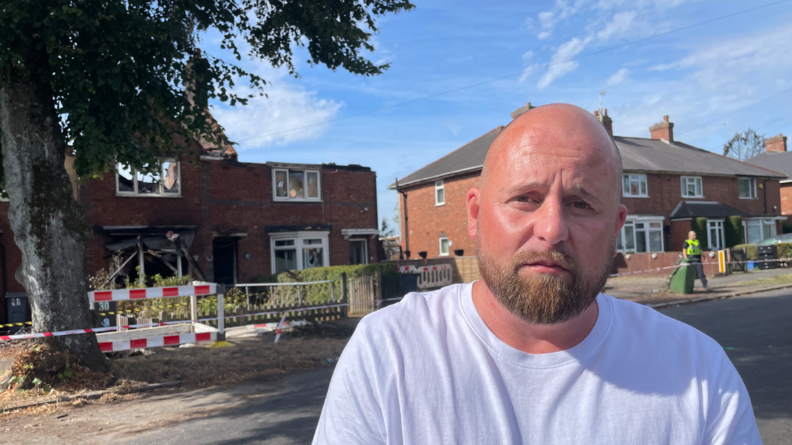 Andrew Reynolds standing in front of a burnt out home 