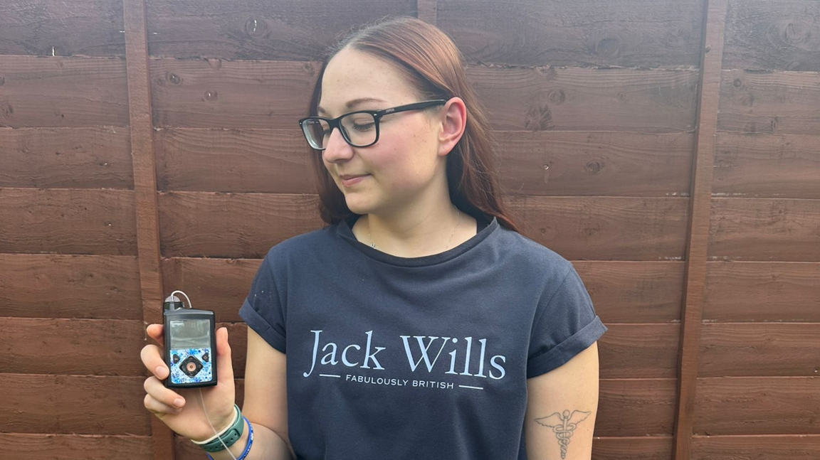 A woman in a blue Jack Wills T-shirt looks down at a pump device she is holding in her right hand.