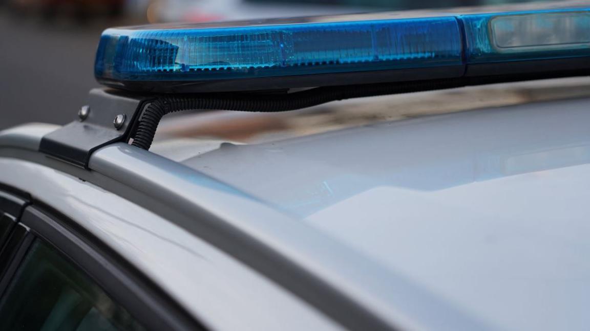 Close-up shot of a police car's blue lights, which are not lit. The roof of the car is white.