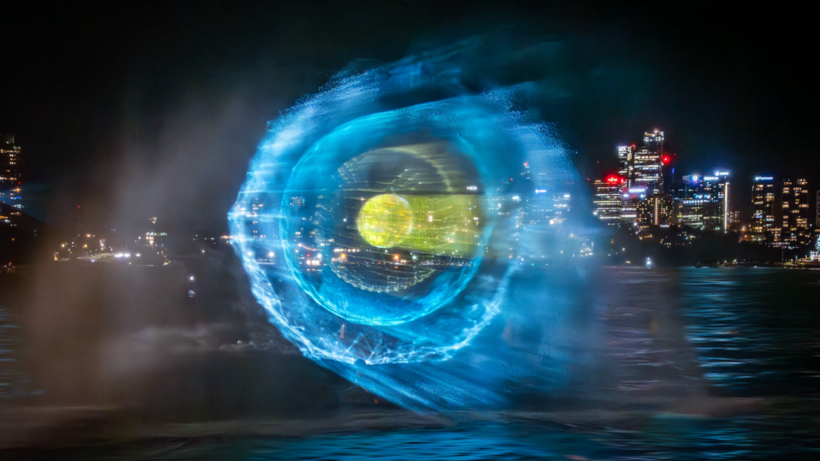 The Manchester skyline is dark and blue light is being projected above the water. 