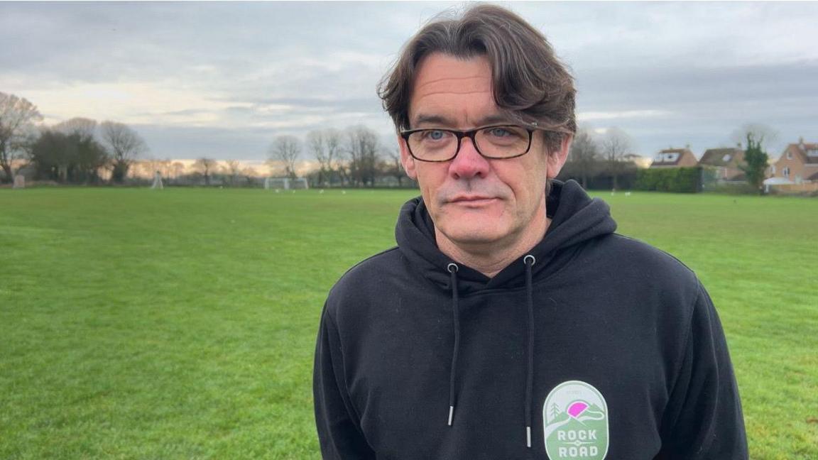 Man wearing glasses and black sweatshirt standing in green field