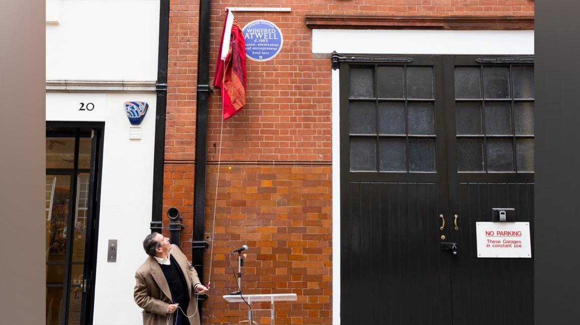 Jools Holland unveils the blue plaque by pulling on some string and revealing it from behind a red curtain