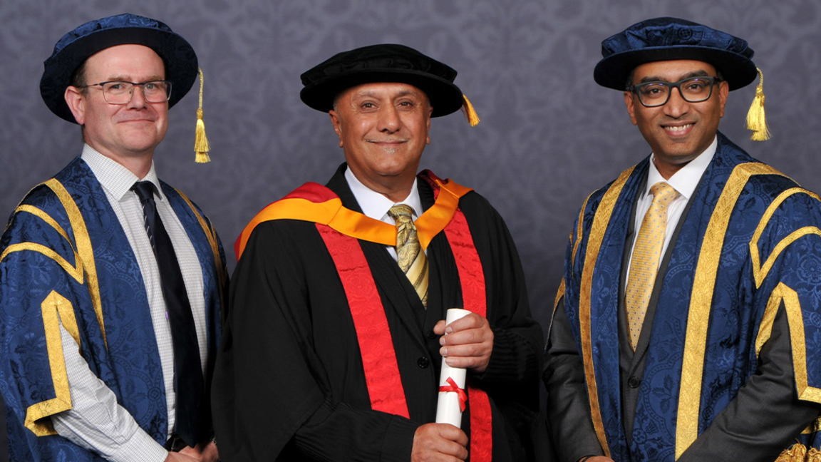 Ranjit Singh Dale in the centre is wearing graduation regalia - a black gown and cap - and is stood in between university representatives