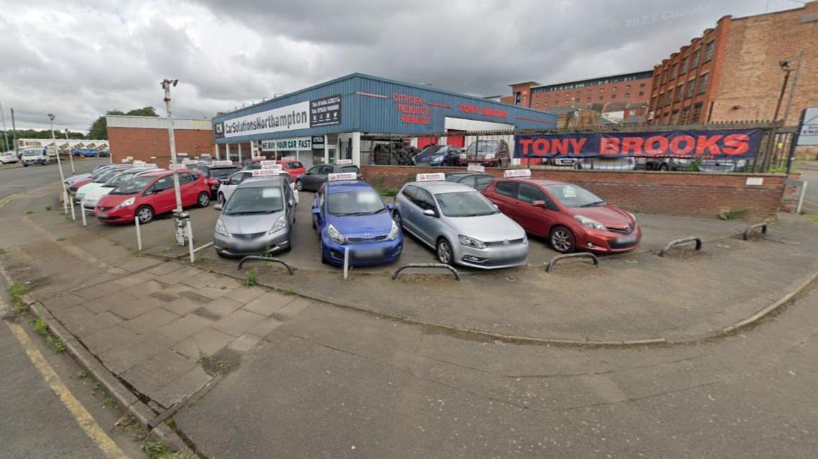 Lots of cars parked outside of a blue corrugated building 