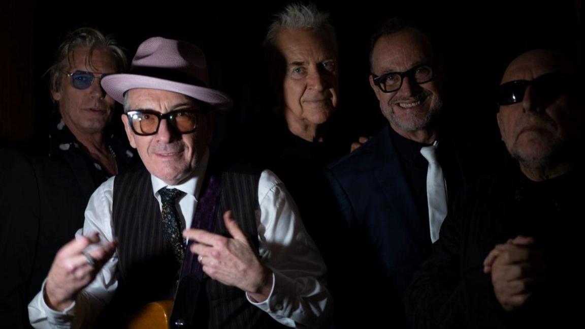 Elvis Costello and The Imposters with Charlie Sexton posing for a publicity image.