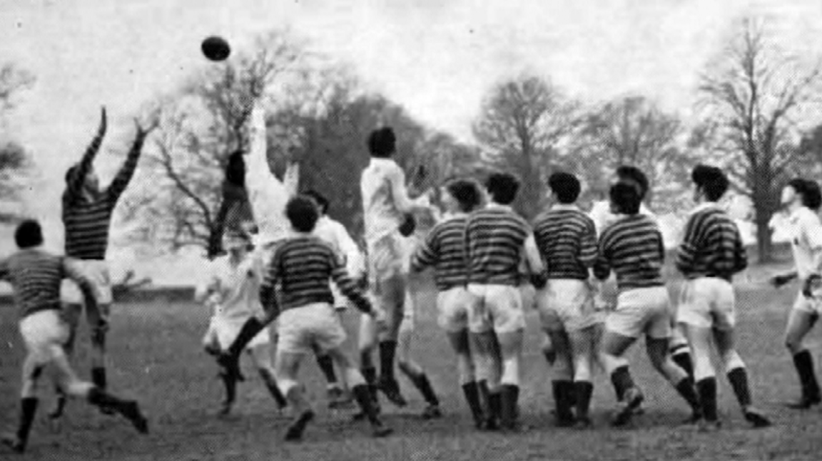 A black and white shot of 15 school boys playing rugby - some in light tops, some in striped