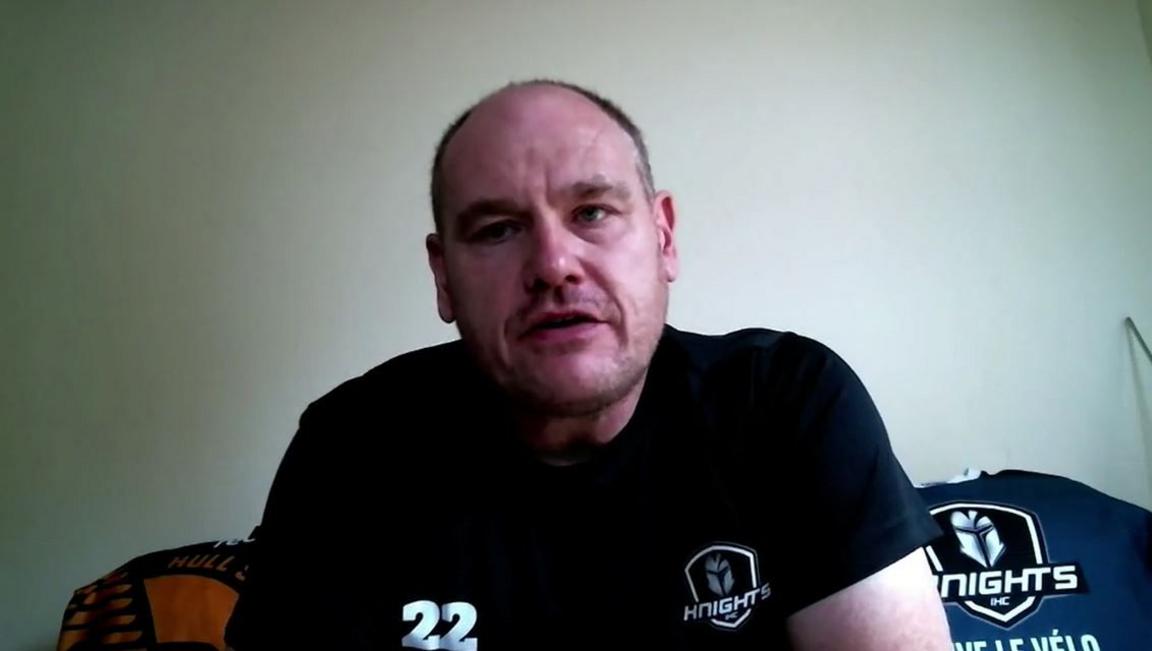 A man with short hair and stubble being interviewed, He is earing a black t-shirt with the number 22 on it and is looking straight at the camera.