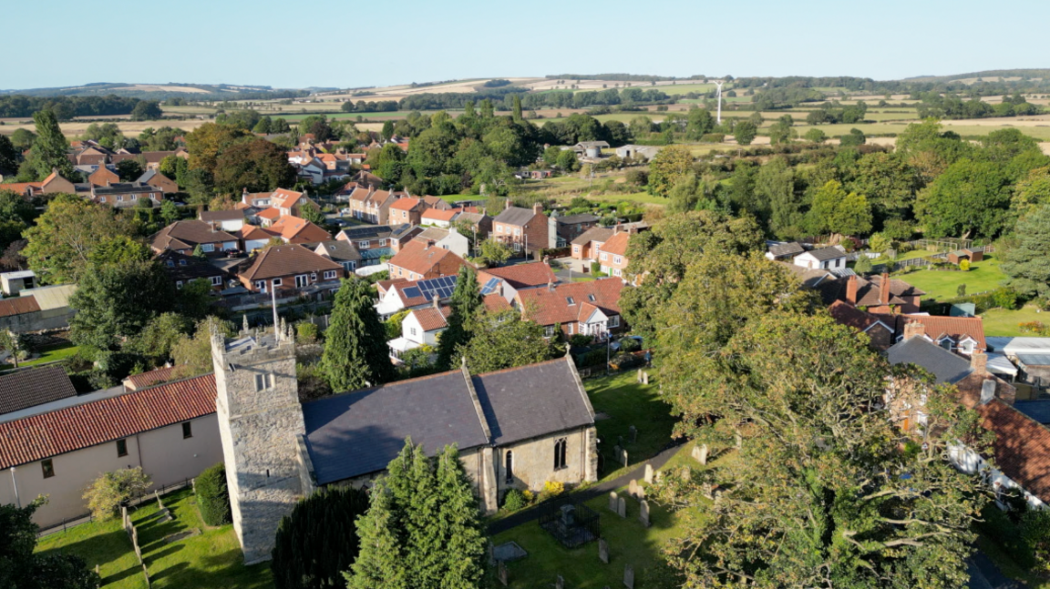 A birds eye view of Shiptonthorpe, focusing in on the village church on a clear sunny day