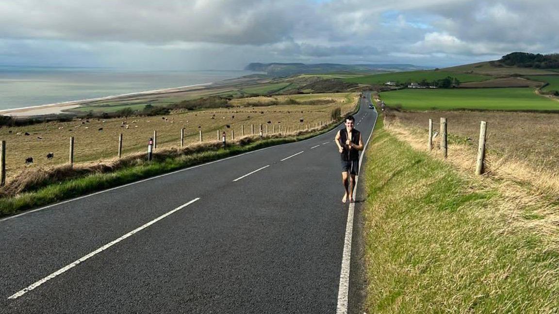 A man running barefoot along a road near the coast