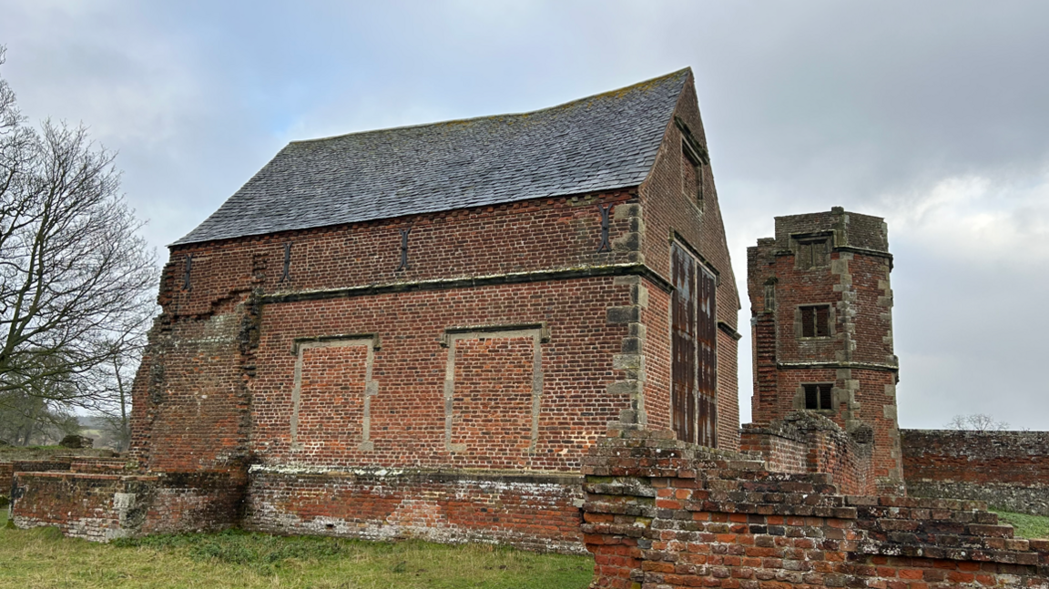 An old brick chapel with a pitched roof - next to a tower and low walls 