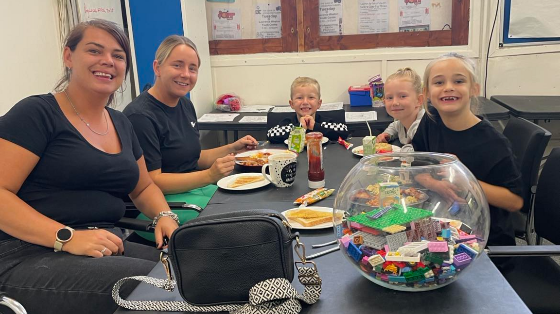 Kids at breakfast club. They are sitting around a table and smiling at the camera