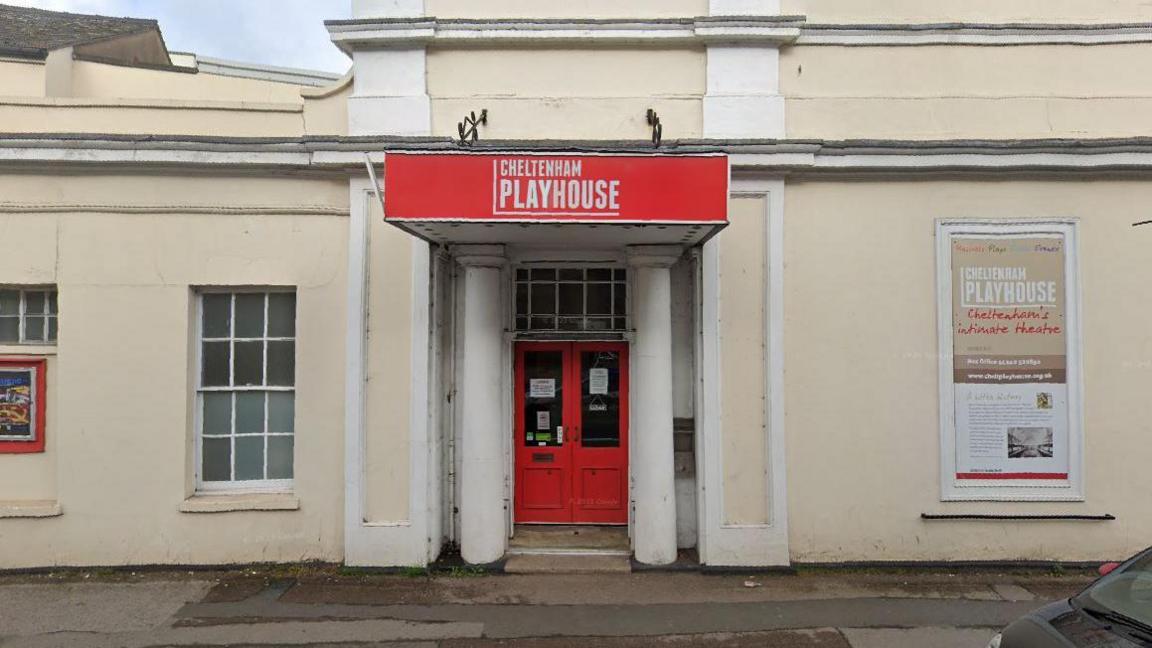 The entrance to Cheltenham Playhouse theatre. It is cream coloured building with a red double door and pillars either side. There is a red sign above it that says 'Cheltenham Playhouse'.