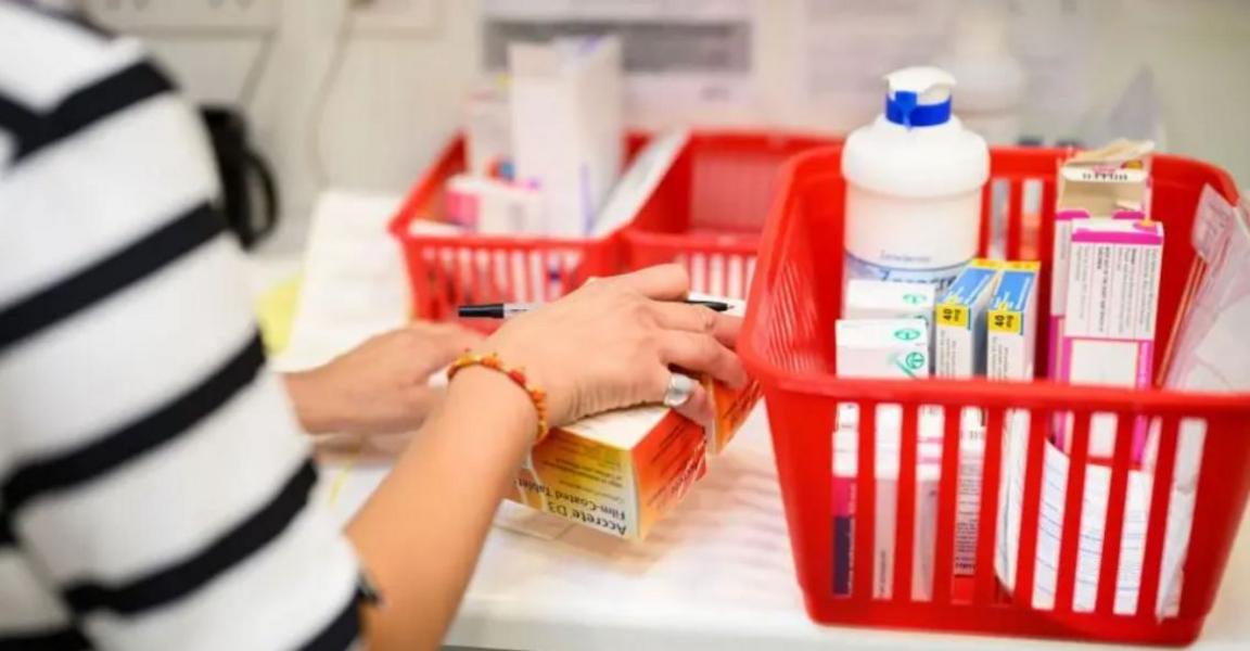 An unidentifiable woman wearing a black and white stripy top, sorting prescriptions into red baskets