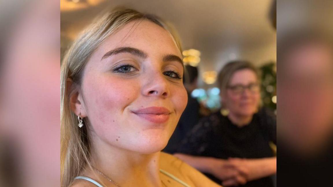 Issy Phipps - a blonde woman with blue eyes - smiles at the camera. She is wearing small gold earrings and a strappy top.