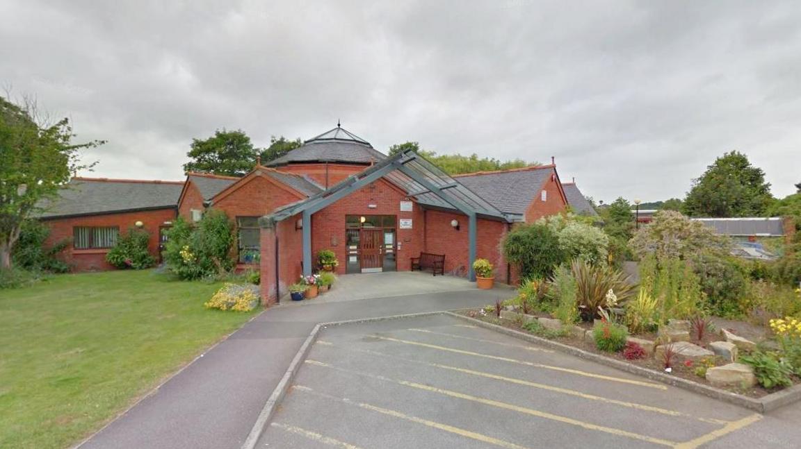 The Langport surgery entrance surrounded by flowerbeds, with a large glass tunnel leading to the front door