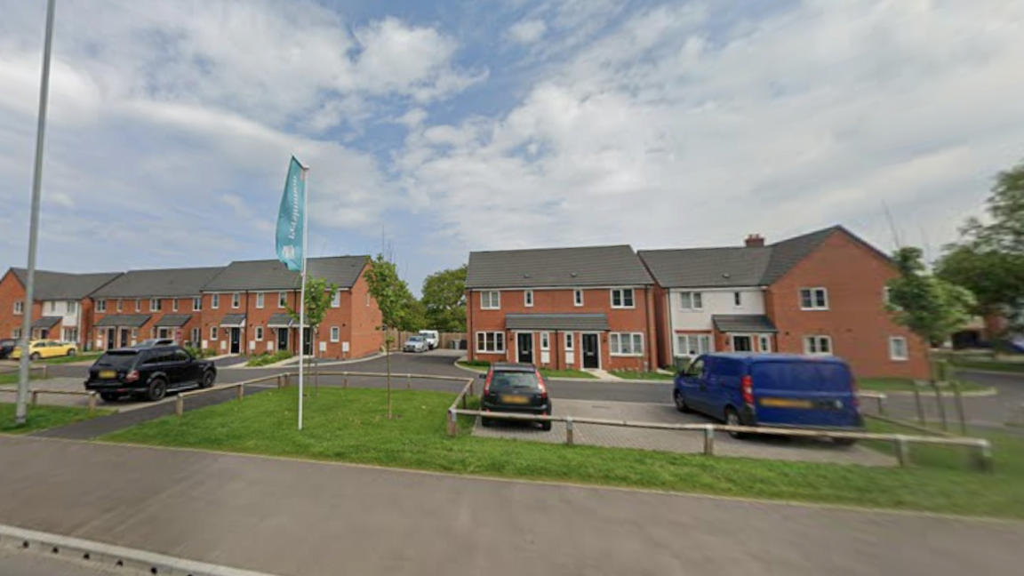 We can see a row of modern houses, with a large cloudy blue sky above them.