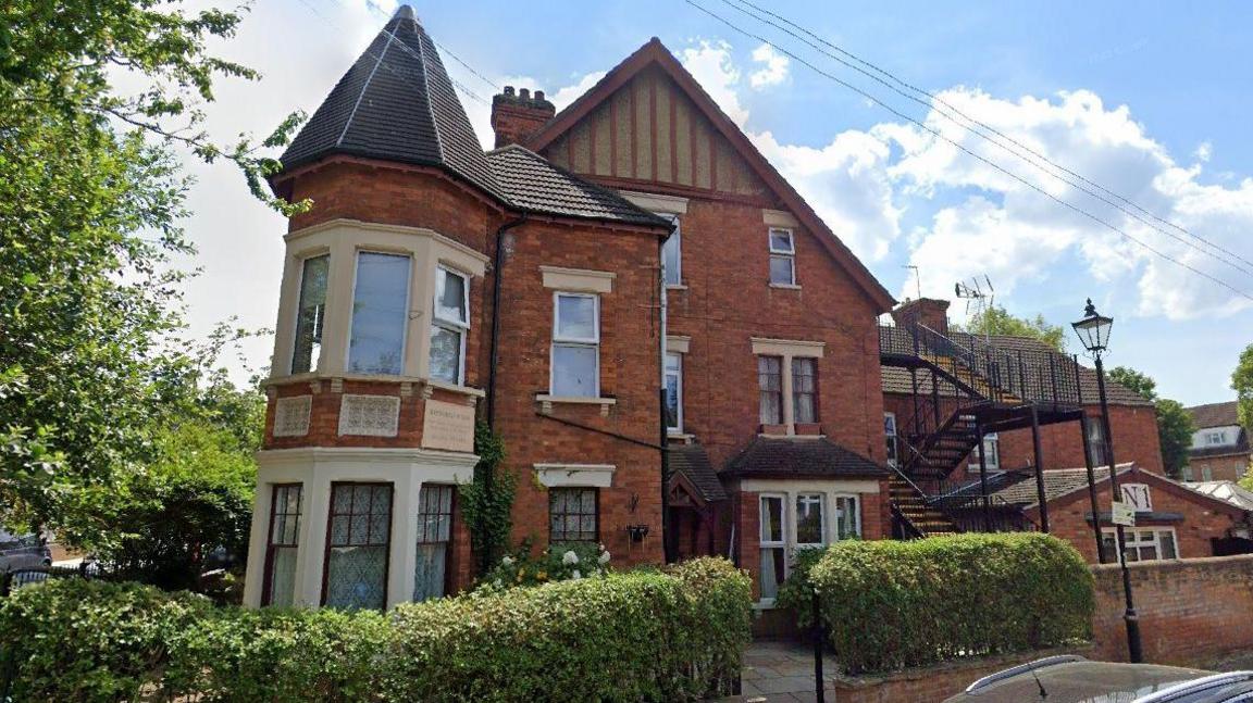 Hepworth House is a large multistory detached house with an iron external staircase. There is a shoulder-high bush surrounding the perimiter