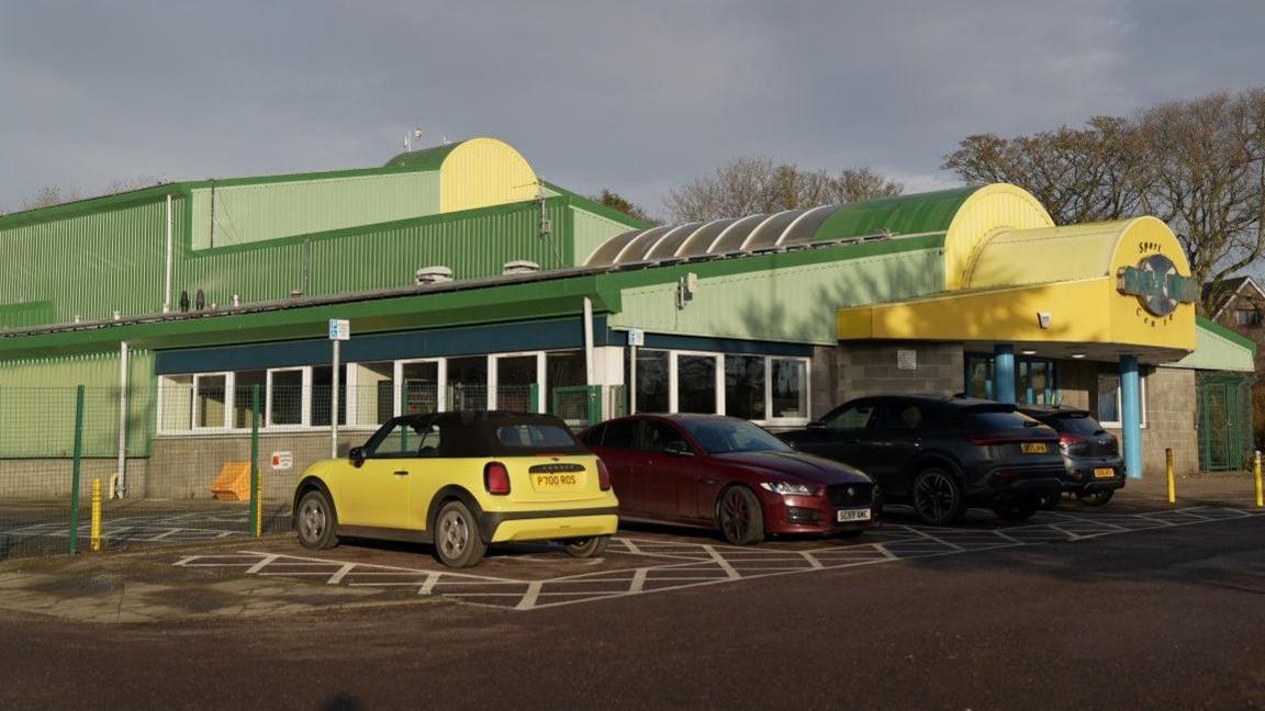 A large green and yellow building that houses the Saltire Centre in Arbroath. Three cars are parked outside the building.