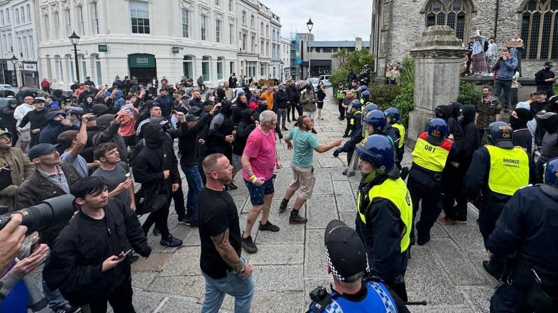 Daniel McGuire in a pink T-shirt and shorts among protesters facing police in Plymouth on Monday