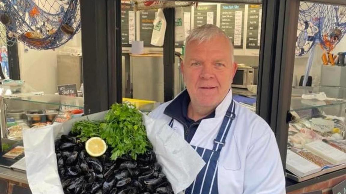 Paul Newberry holding a box of muscles while standing outside his the Fish Box shop.