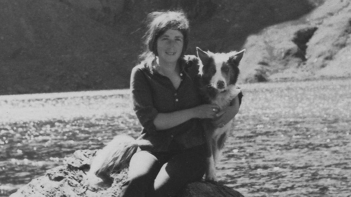 A black and white photo of Ginny and her dog Jester sitting on a  rock next to the sea.