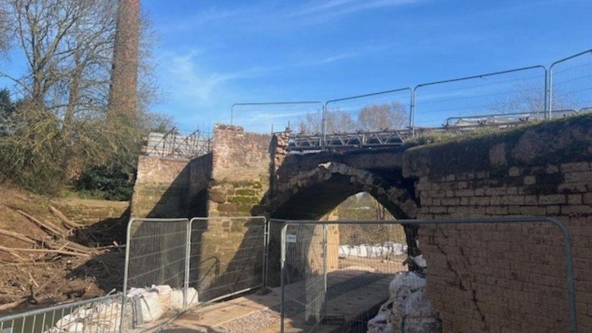 Closed bridge, with barriers on top of it and also near it close to the bottom of the bridge by the river.