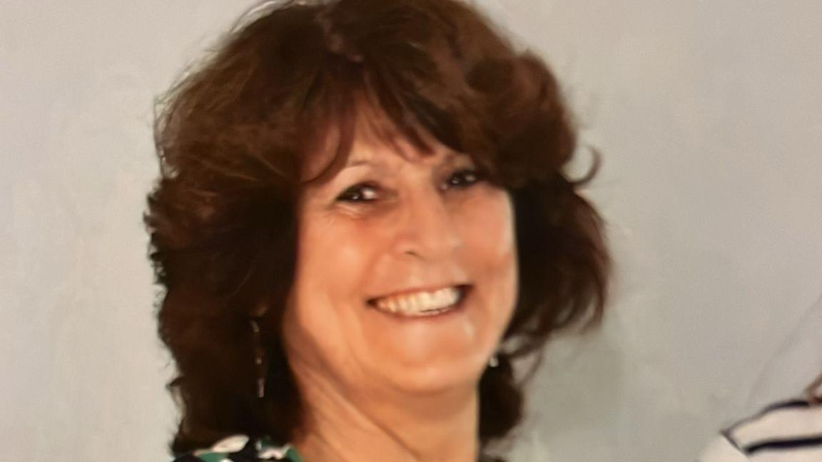 Pamela Arthur smiles at the camera. She has voluminous brown hair and a beaming smile.