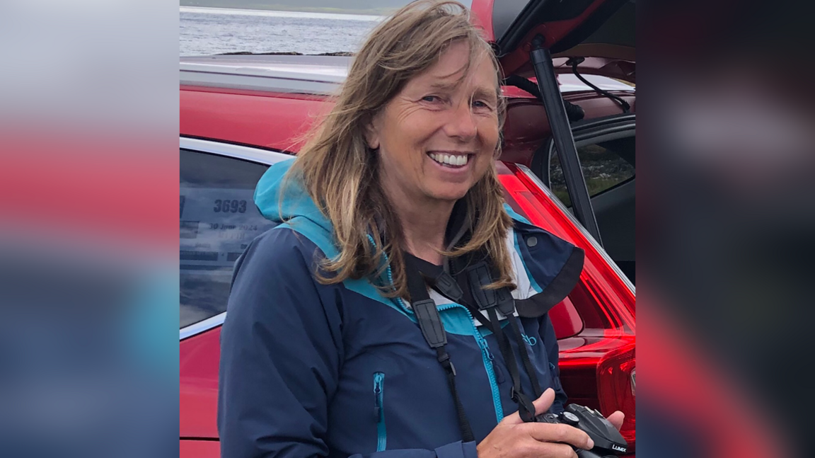 Jenny Hobson standing in front of a red car and holding a camera