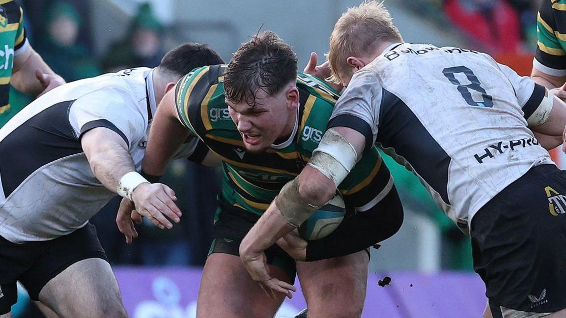 Jack Lewis tries to force his way through tackles by two Saracens players