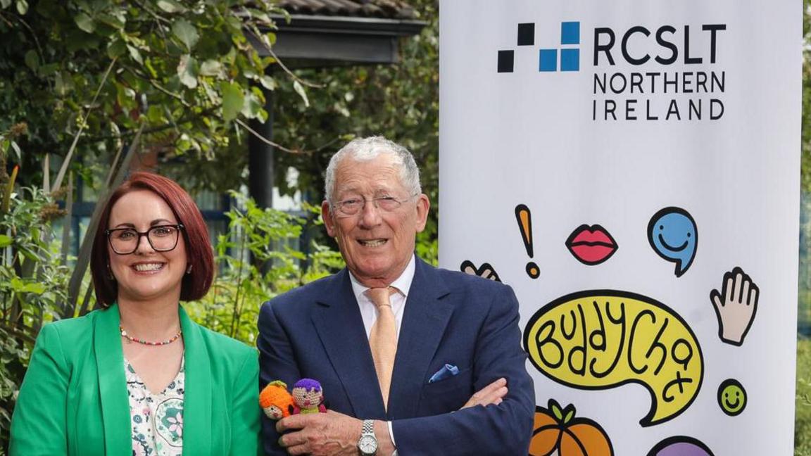 Ruth Sedgewick and Nick Hewer with a banner for RCSLT Northern Ireland in the background 