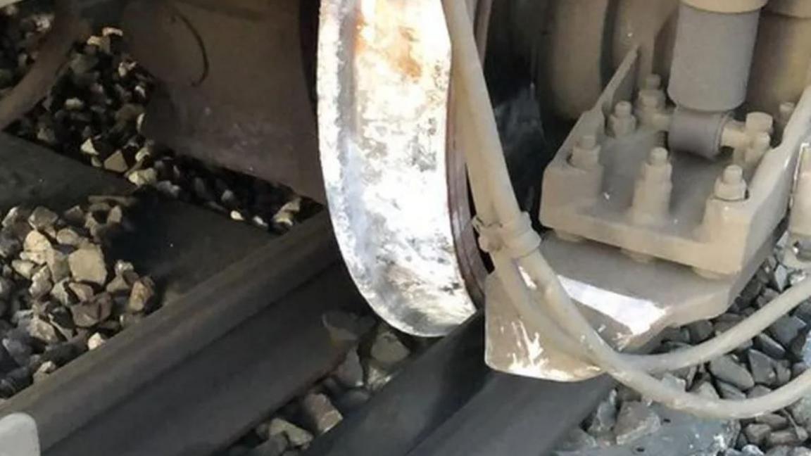 A silver damaged wheel of a train. 