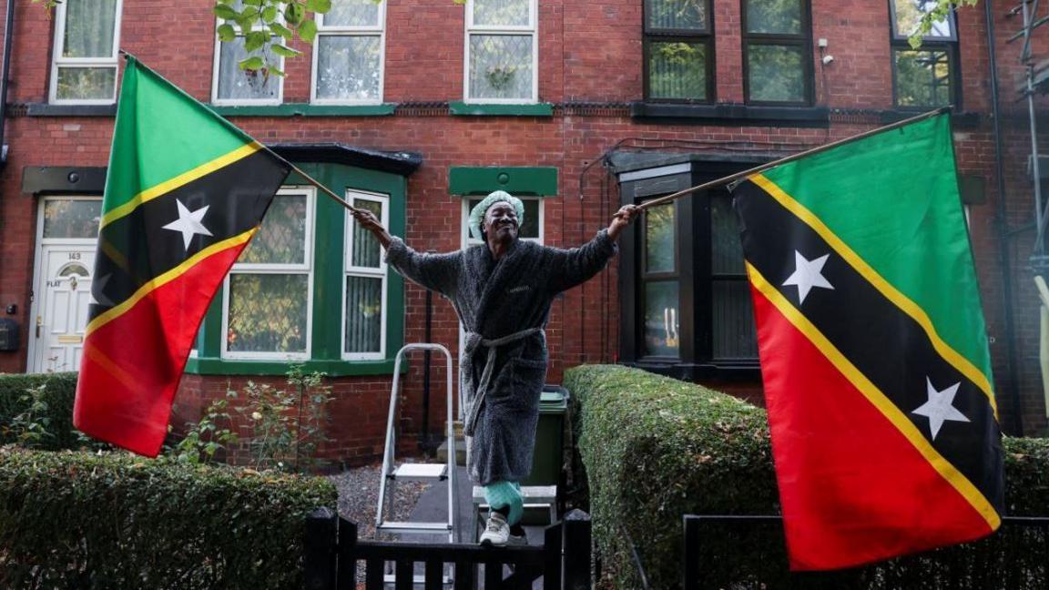 A Leeds woman holds up St. Kitts and Nevis flag in the J'Ouvert celebrations at sunrise before Leeds West Indian Carnival 2025 in Chapeltown