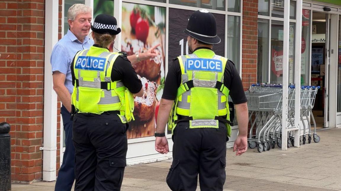 Two police officers talk to a member of the public outside a shop