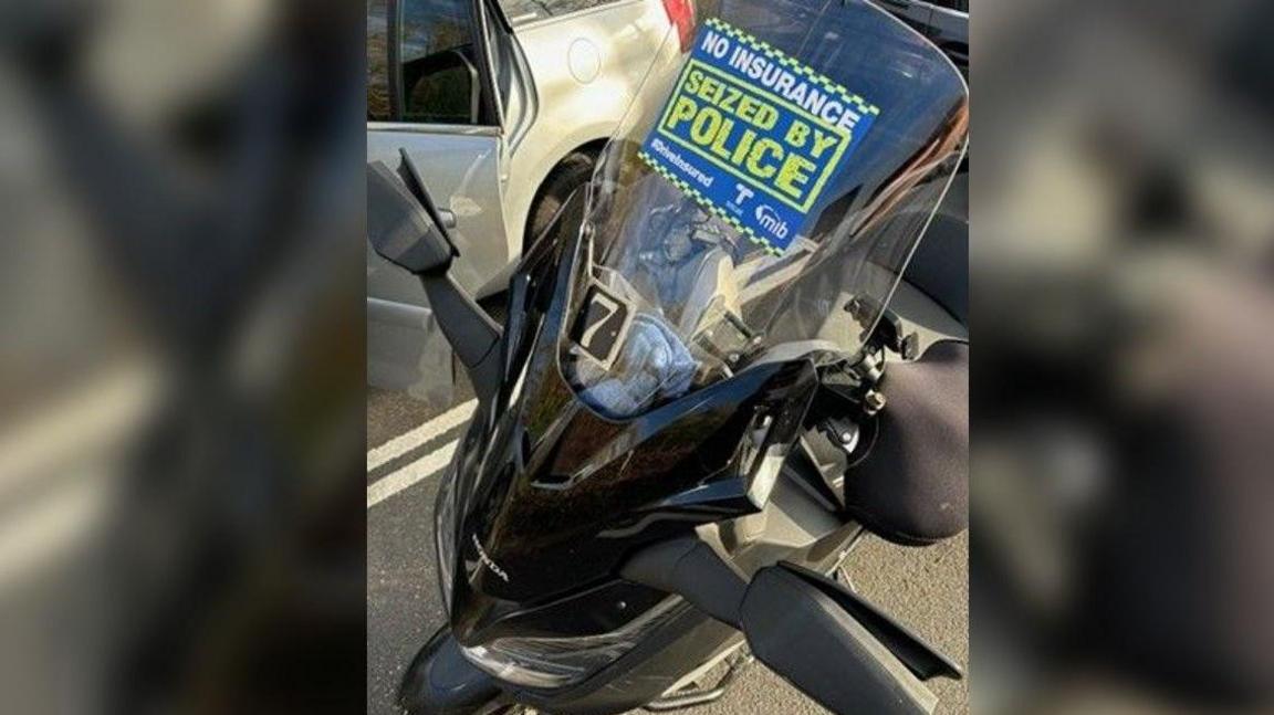 Seized black motorcycle parked on concrete with vehicles in the background.