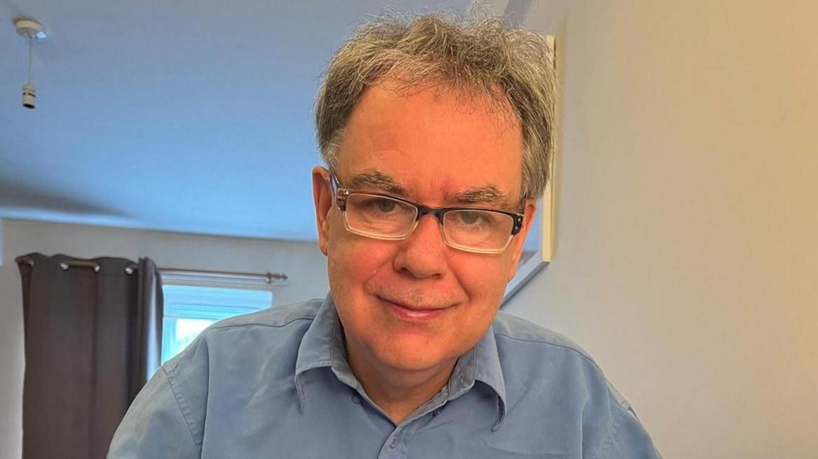 Julian Watson smiling while wearing glasses and a blue shirt