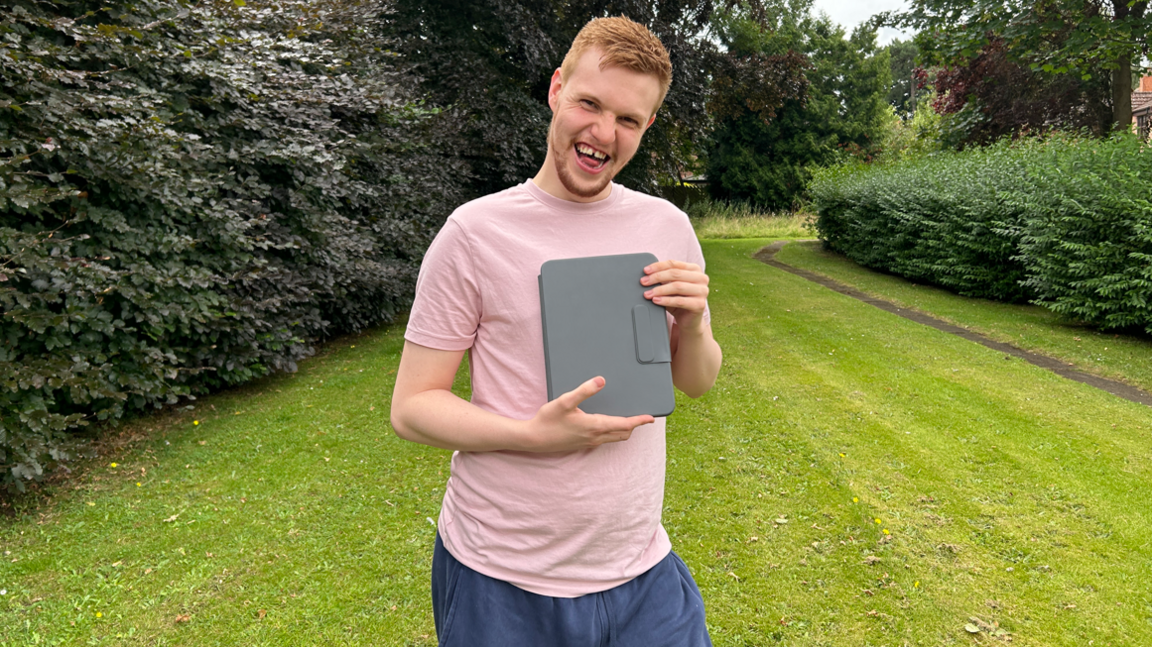 Man wearing pink t-shirt in a back garden while holding an ipad 