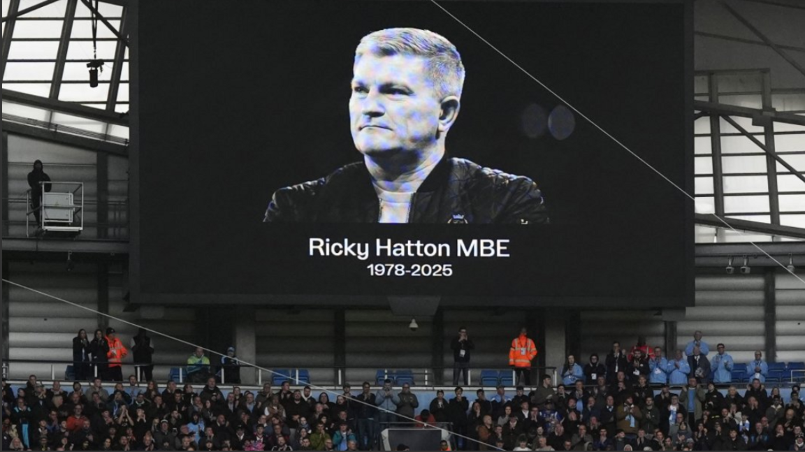 A black and white image of Ricky Hatton is projected above Manchester City fans and stewards at a stand at the Etihad stadium.