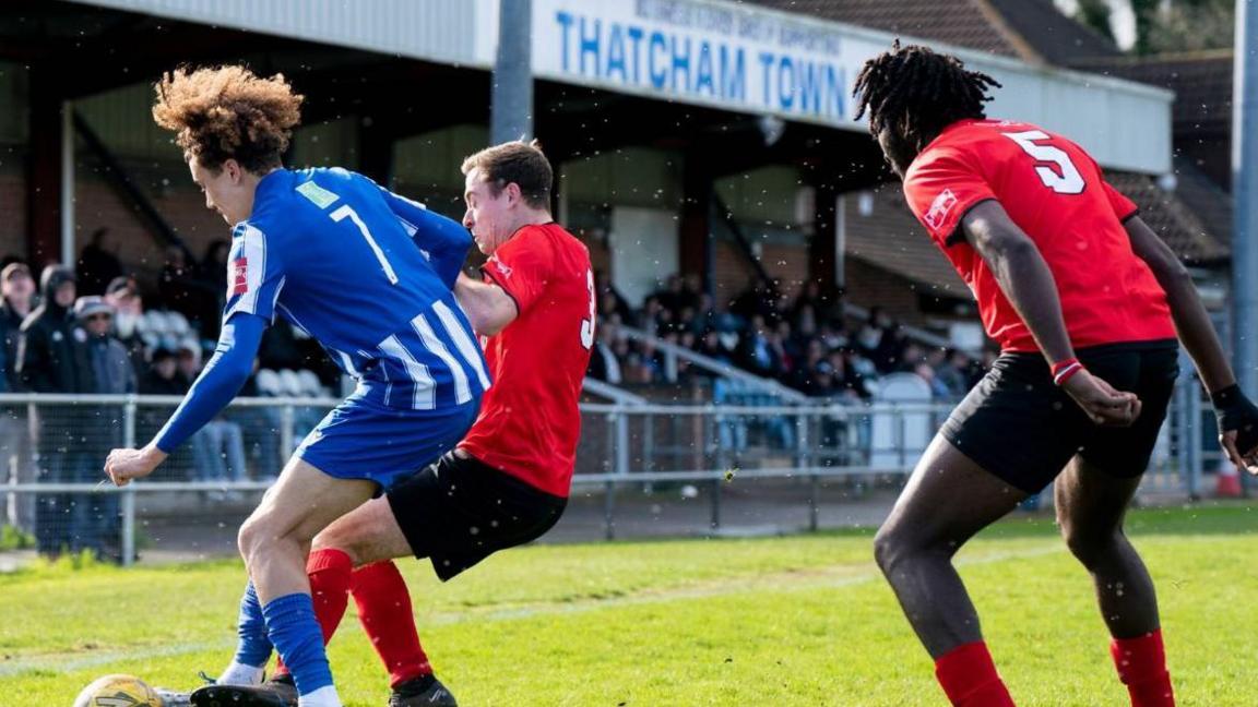 A Thatcham player - white, with curly hair - is challenged by an opposition player - white with dark hair - at Thatcham Town's Waterside Park ground 