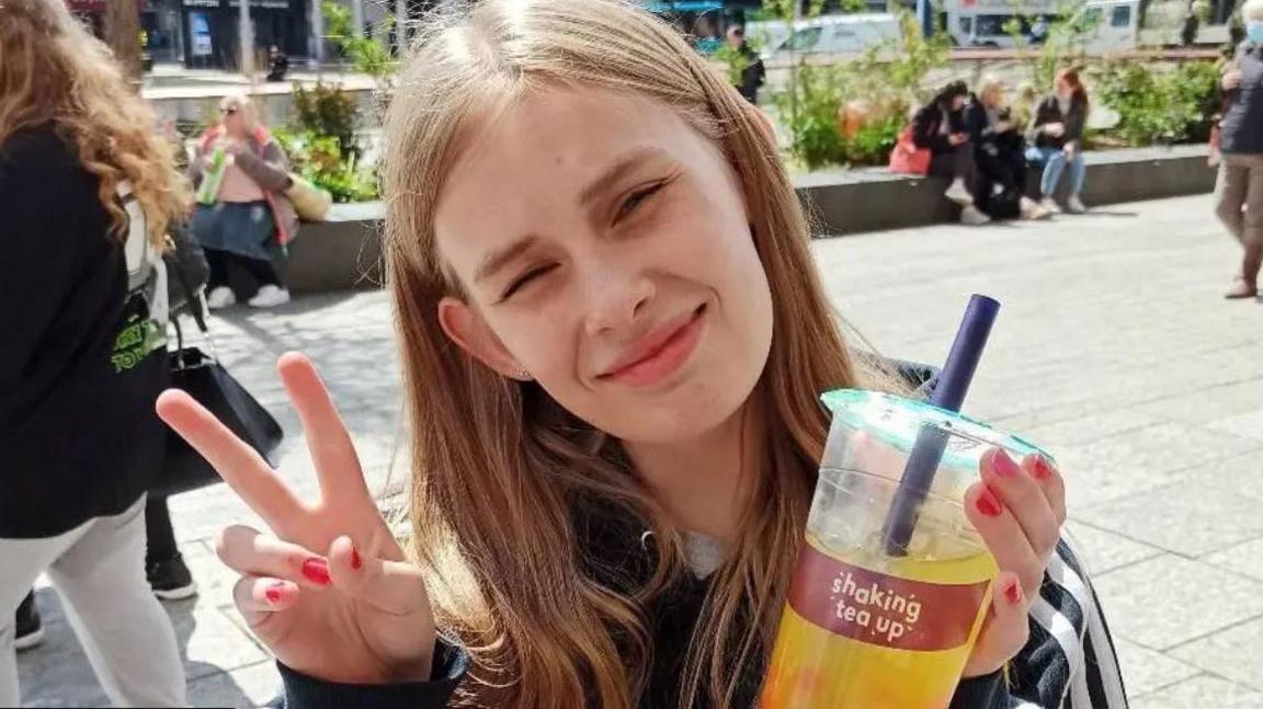 Rhianan Rudd holding up a bubble tea and giving a peace sign to the camera