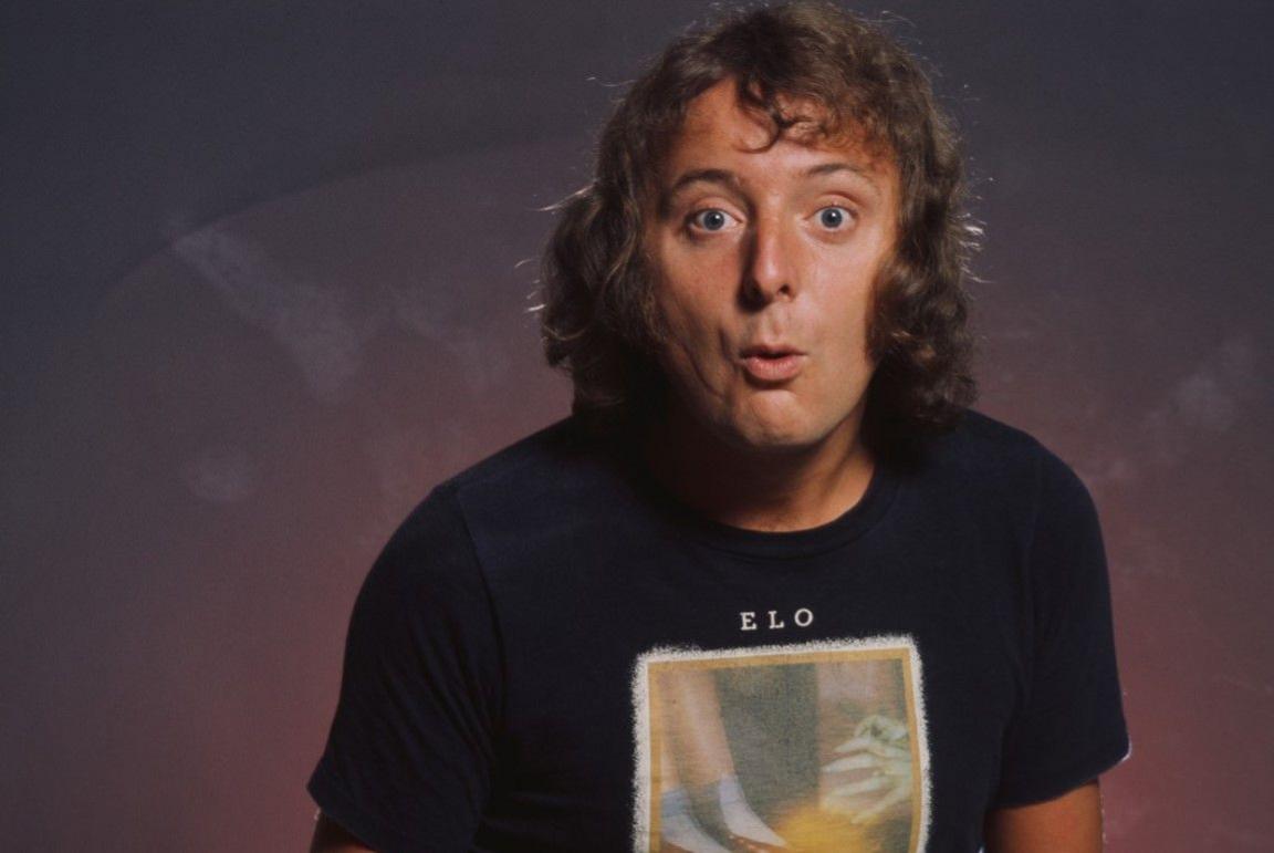 Jasper Carrott, with curly hair, wearing a largely black T-shirt, with ELO named on it.