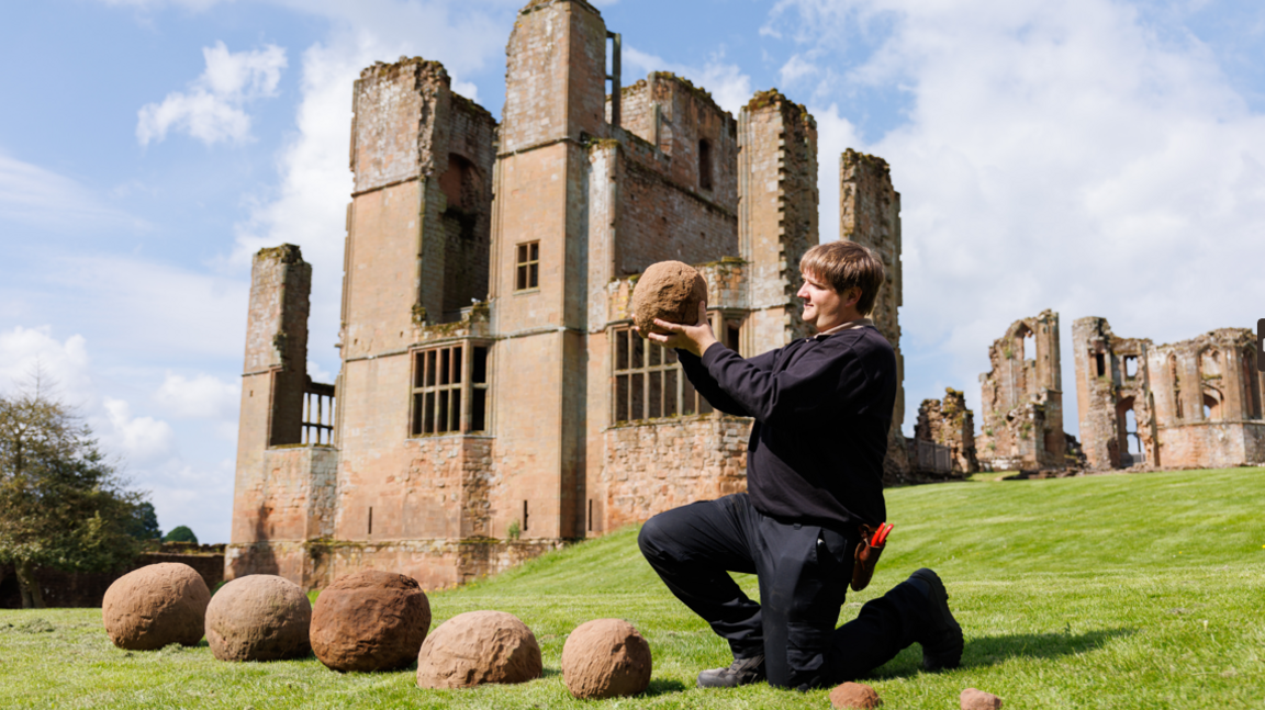 The catapult shots lined up in front of the castle, with a man holding one of them