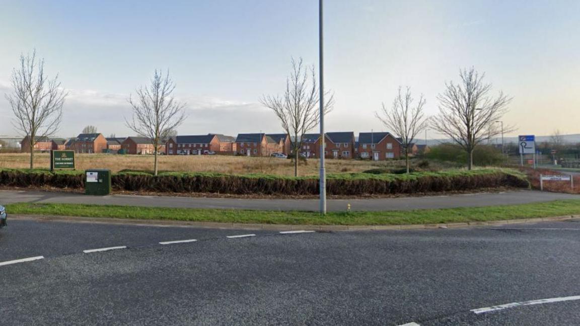 Land off Sir Isaac Newton Way in Rochdale showing five trees and a housing development in the background