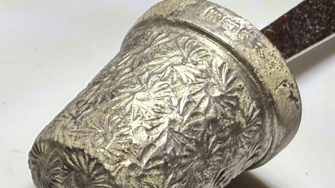 A silver thimble is displayed on the end of a pen.