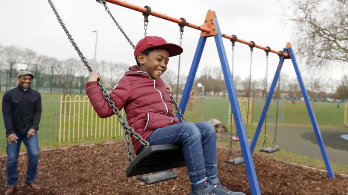 Boy smiling on the swing and his father behind smiling 