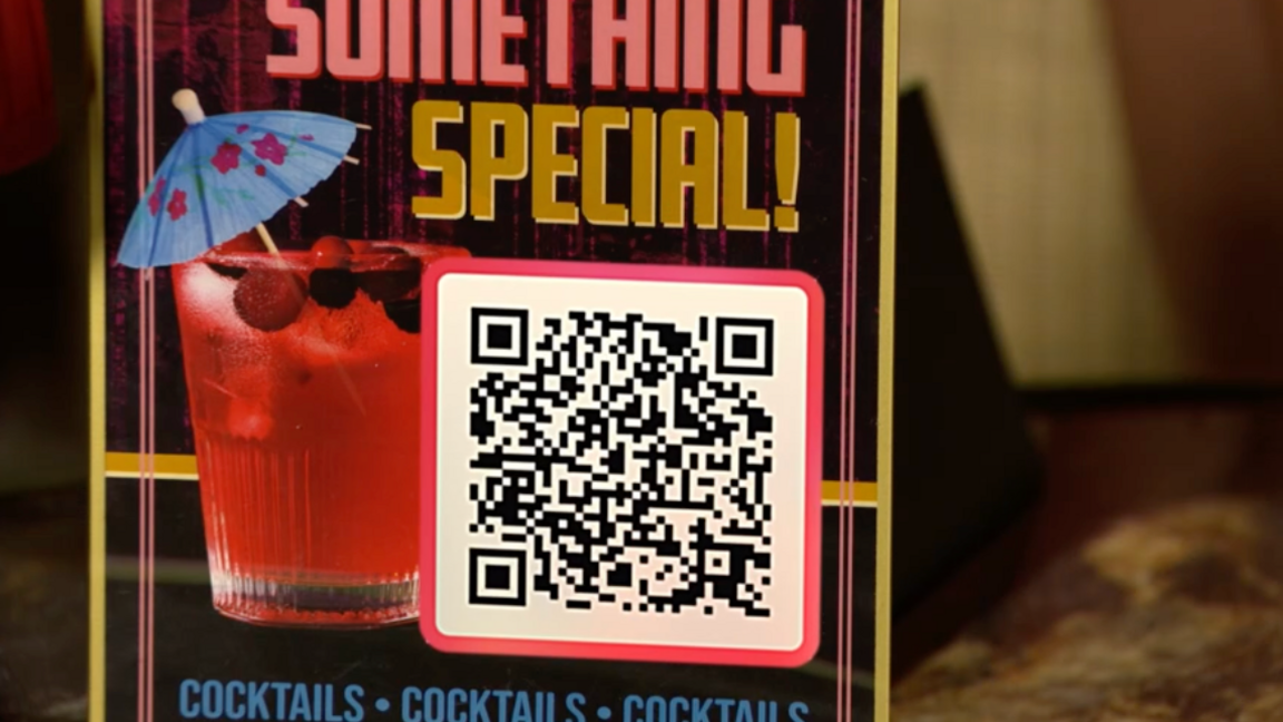 A close-up of a drinks menu on a table with a picture of a pink cocktail with a paper umbrella in it. Under the words "Something special!" a square with a QR code inside it is visible.