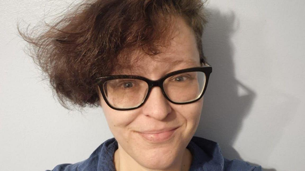 A woman wearing black glasses and a navy shirt smiling while looking straight at the camera.