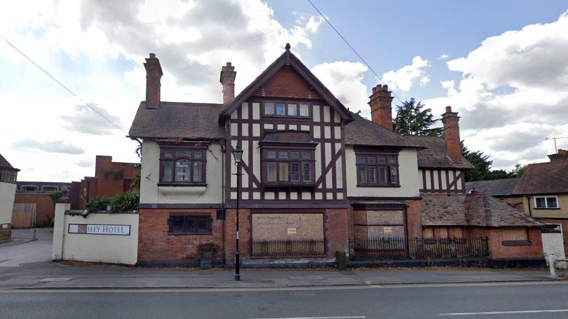 The Allesley Hotel, a cream and maroon striped building, with boarded up windows.